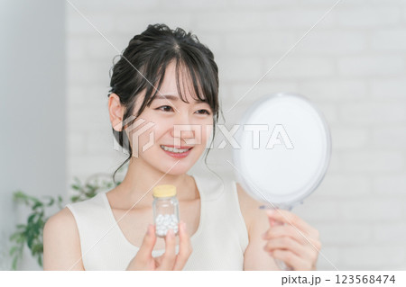 鏡を見ながら薬・サプリメントの瓶を持つ笑顔のアジア人女性 鏡を見ながら薬・サプリメントの瓶を持つ笑顔のアジア人女性 123568474