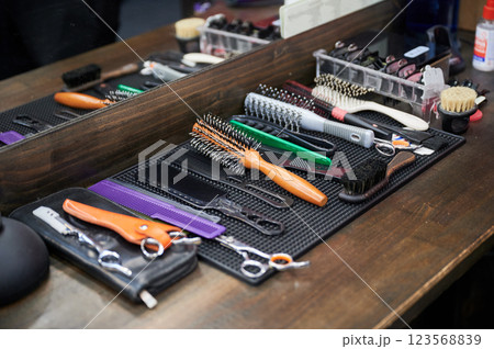 Close up view of hairdresser's tools. Cropped photo of barber's equipment on wooden table. Different combs and brushes lying on background of mirror. 123568839