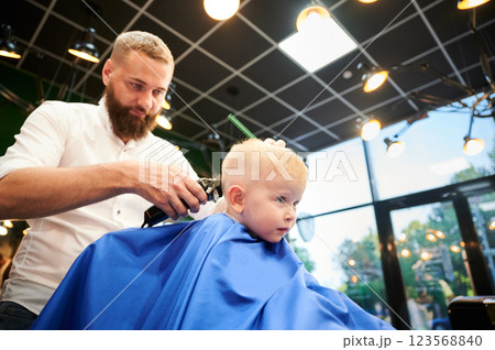 Barber using comb and shaver to cut hair. Professional hairdresser shaving little kid's nape. Close up. Barber using comb and shaver to cut hair. Professional hairdresser shaving little kid's nape. Close up. 123568840
