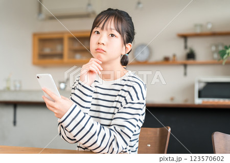 自宅のリビング・ダイニングでスマホを使う小学生・中学生の女の子 自宅のリビング・ダイニングでスマホを使う小学生・中学生の女の子 123570602