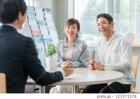 ショールーム・商談スペースで話を聞く夫婦と接客するビジネスマン ショールーム・商談スペースで話を聞く夫婦と接客するビジネスマン 123571378