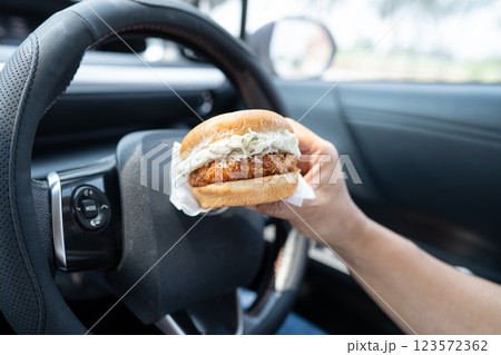 Asian lady holding hamburger to eat in car, dangerous and risk an accident. Asian lady holding hamburger to eat in car, dangerous and risk an accident. 123572362
