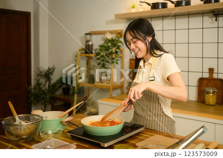 Happy young woman enjoys preparing a homemade spaghetti meal in her modern kitchen Happy young woman enjoys preparing a homemade spaghetti meal in her modern kitchen 123573009