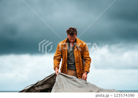 Young man sets up temporary tent in disaster area under overcast sky 123574390