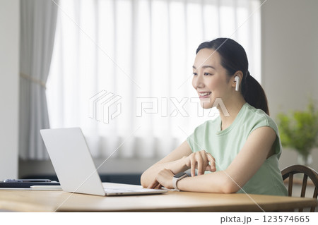 イヤホンをつけてノートパソコンに向かう30代の女性　オンラインミーティング　ビデオチャット　イメージ 123574665