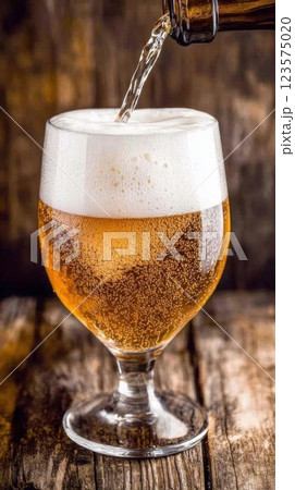 Frothy beer poured into a glass with foam spilling at a rustic wooden bar setting 123575020