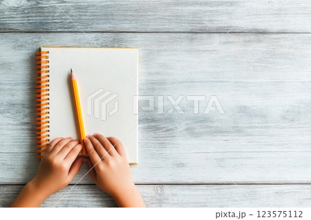Childs hands hold a new pencil above a blank notebook ready for creative expression 123575112