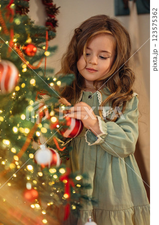 Beautiful little girl decorates a christmas tree 123575362