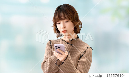 スマートフォンを見て考える女性・ビジネスウーマン スマートフォンを見て考える女性・ビジネスウーマン 123576104
