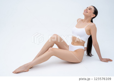 Sweet long-haired slim woman in white lingerie sitting on floor and smiling nicely 123576109