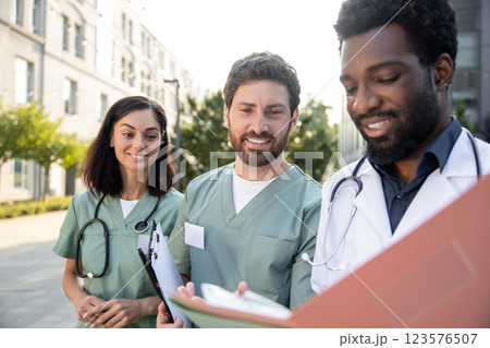 Group of young doctors in a clinic yard discussing patient case and looking interested Group of young doctors in a clinic yard discussing patient case and looking interested 123576507