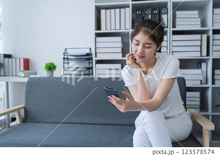Woman is sitting on a couch using a smartphone and engaging in social media while enjoying a relaxing moment at home 123578574