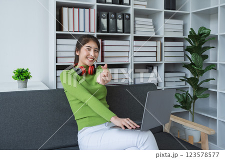 Woman with make mini heart symbol, wearing headphones using her computer enjoying music at home Woman with make mini heart symbol, wearing headphones using her computer enjoying music at home 123578577