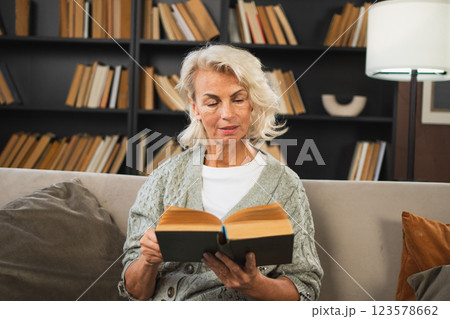 Comfort relaxed senior old elderly woman reading book at home. Mature woman resting enjoy calm day sitting on sofa at home alone. Adult lady spending free time keeping book smiling. Pension concept 123578662