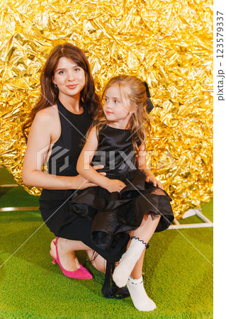mother and daughter in black dresses against the background of a golden wall. 123579337