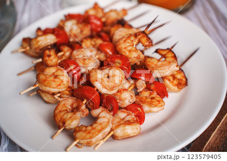 Skewers with shrimps and tomatoes on a white plate.  123579405