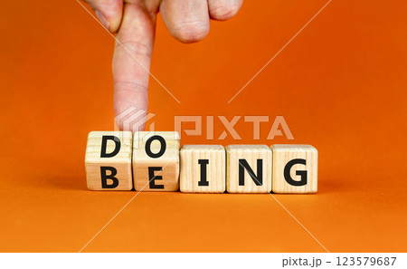 Doing or being symbol. Concept word Doing and Being on wooden cubes. Businessman hand. Beautiful orange table orange background. Business doing or being concept. Copy space. 123579687