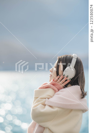 湖の波打ち際でヘッドホンで音楽を聴いている若い女性 123580874