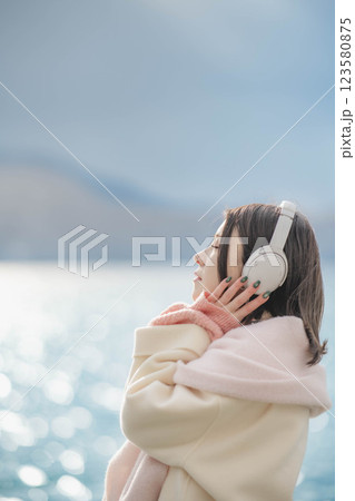 湖の波打ち際でヘッドホンで音楽を聴いている若い女性 湖の波打ち際でヘッドホンで音楽を聴いている若い女性 123580875