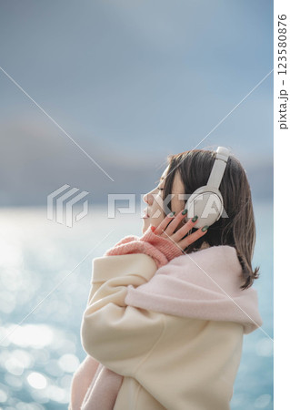 湖の波打ち際でヘッドホンで音楽を聴いている若い女性 湖の波打ち際でヘッドホンで音楽を聴いている若い女性 123580876