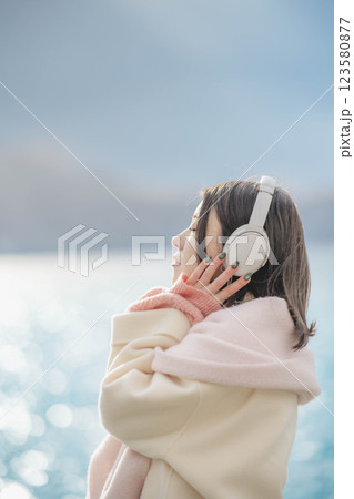湖の波打ち際でヘッドホンで音楽を聴いている若い女性 湖の波打ち際でヘッドホンで音楽を聴いている若い女性 123580877