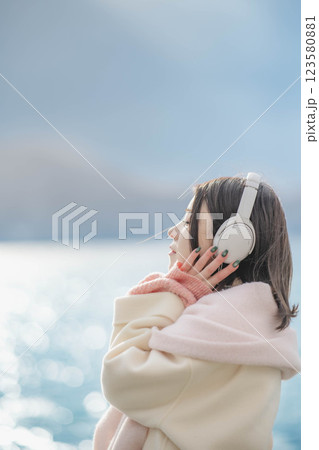 湖の波打ち際でヘッドホンで音楽を聴いている若い女性 123580881