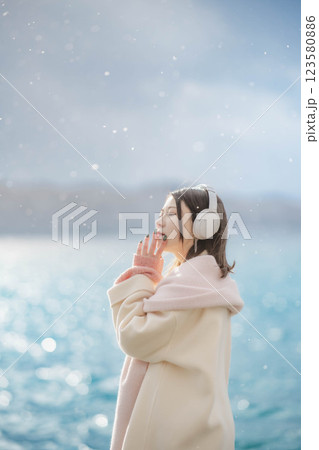 湖の波打ち際でヘッドホンで音楽を聴いている若い女性 123580886