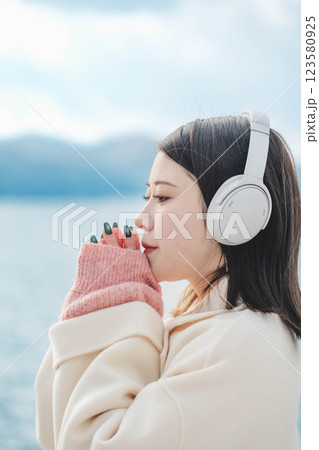 湖の波打ち際でヘッドホンで音楽を聴いている若い女性 123580925