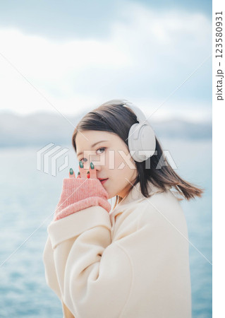 湖の波打ち際でヘッドホンで音楽を聴いている若い女性 123580931