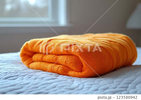 Folded orange knitted blanket on a white bed Folded orange knitted blanket on a white bed 123580942