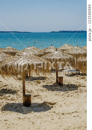 Straw umbrellas on sandy beach with turquoise sea in background. Tropical style summer retreat with exotic resort atmosphere. .Quiet beach with straw umbrellas, sunny day by turquoise sea 123580984