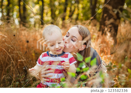 Young mother and her one-year-old baby taking pictures in autumn park bushes 123582336