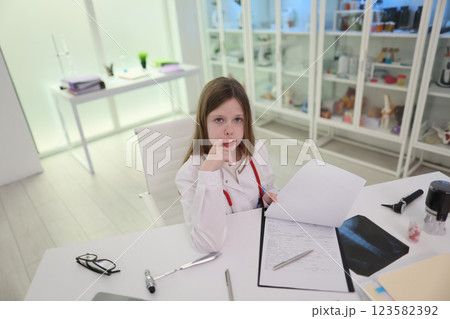 A young girl is in a bright, modern workspace, surrounded by documents, showing her focus 123582392