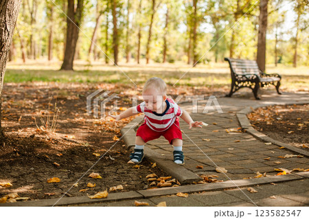 Baby boy in red summer outfit learning to walk outdoors in the park Baby boy in red summer outfit learning to walk outdoors in the park 123582547