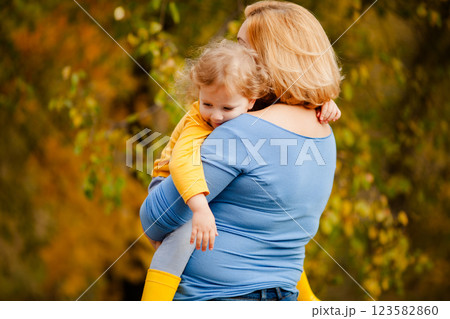 Loving mother holding toddler girl with curly hair in yellow shirt in autumn park 123582860