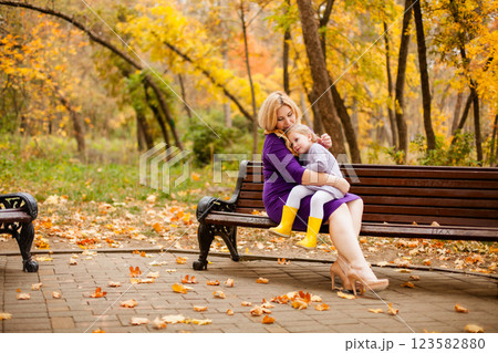 Loving mother in purple dress hugging her sad daughter on park bench 123582880