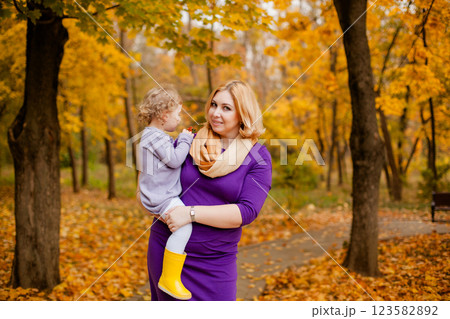 Plus-size woman in purple dress holding and playing with her 3-year-old daughter in autumn park 123582892