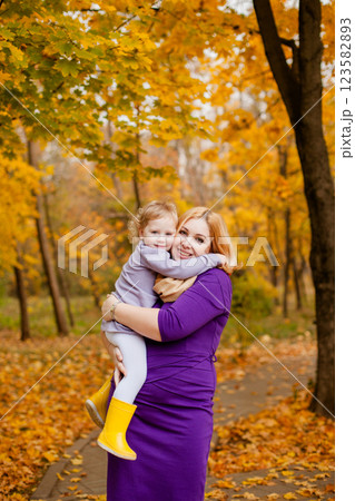 Plus-size woman in purple dress holding and playing with her 3-year-old daughter in autumn park Plus-size woman in purple dress holding and playing with her 3-year-old daughter in autumn park 123582893