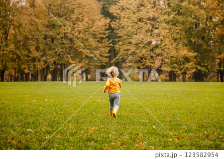 Toddler girl with curly hair in a yellow shirt playing in an autumn park Toddler girl with curly hair in a yellow shirt playing in an autumn park 123582954