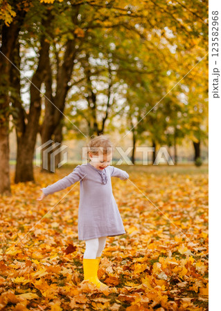Toddler girl in purple dress, white tights, and yellow rubber boots playing happily with leaves in autumn park Toddler girl in purple dress, white tights, and yellow rubber boots playing happily with leaves in autumn park 123582968