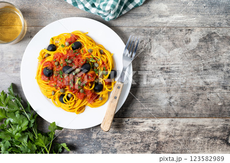 Italian Pasta puttanesca with tomato sauce, capers, and black olives on wooden table. Top view. Copy space 123582989