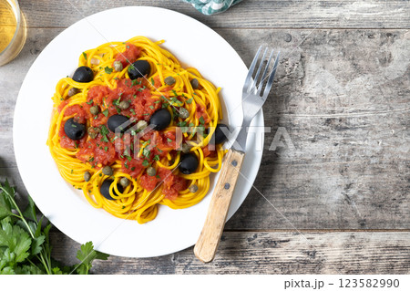 Italian Pasta puttanesca with tomato sauce, capers, and black olives on wooden table. Top view. Copy space 123582990