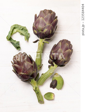 Whole purple raw roman artichokes on a white wooden table top view. Fresh italian vegetables 123584404