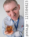 A drunk doctor looks at a glass of alcohol with a grimace of disgust. Close-up wide-angle shot 123584823