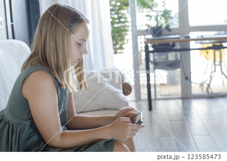 Pensive little girl with smartphone watching cartoons or playing mobile games at home Pensive little girl with smartphone watching cartoons or playing mobile games at home 123585473