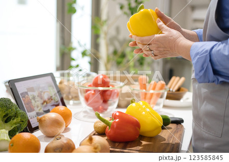 タブレットを見ながら料理をするミドル女性 123585845