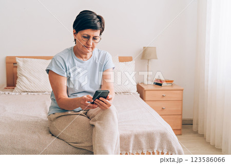 Mature caucasian woman using smartphone in bedroom for messaging and relaxation 123586066