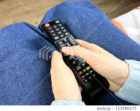 Girl presses button on TV controller while watching her favorite show. Control your TV using wireless remote control. Convenient device for wirelessly changing channels on your TV at home 123586275