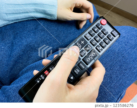 Girl turns down sound of TV using remote control, watching TV at low volume. Using the remoter to control audio noise from the TV, girl presses button on the TV remote control 123586276