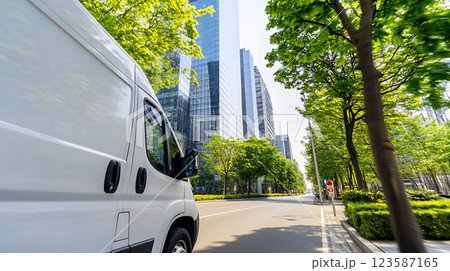 White Cargo Van Driving Through Modern City with Glass Skyscrapers and Greenery 123587165